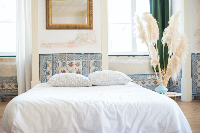 Big bed with white linens near the table with a vase