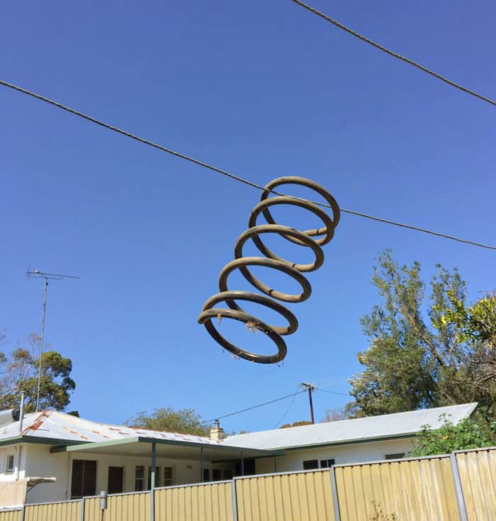 Garden hose humorously tangled in a coil on a wire, with a house and trees in the background, showcasing parents' sense of humor.