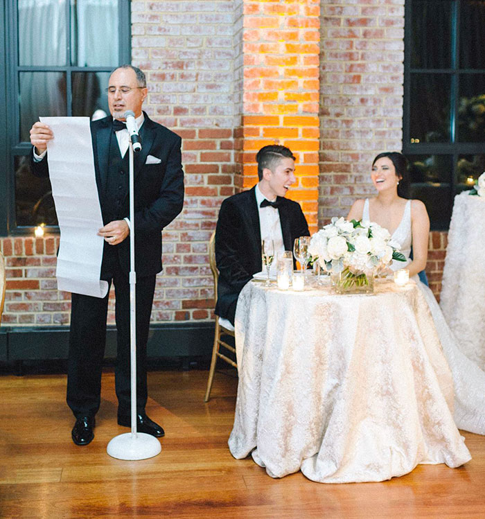 Father with long speech paper humorously addresses newlyweds at the wedding reception.