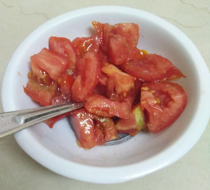 Chopped tomatoes in a white bowl with fork, showcasing parents’ humor in food presentation.