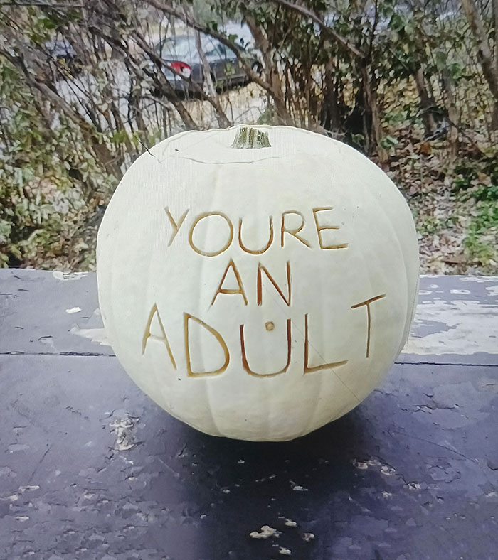 Pumpkin carved with "YOU'RE AN ADULT" showcasing parents' humorous message in a garden setting.