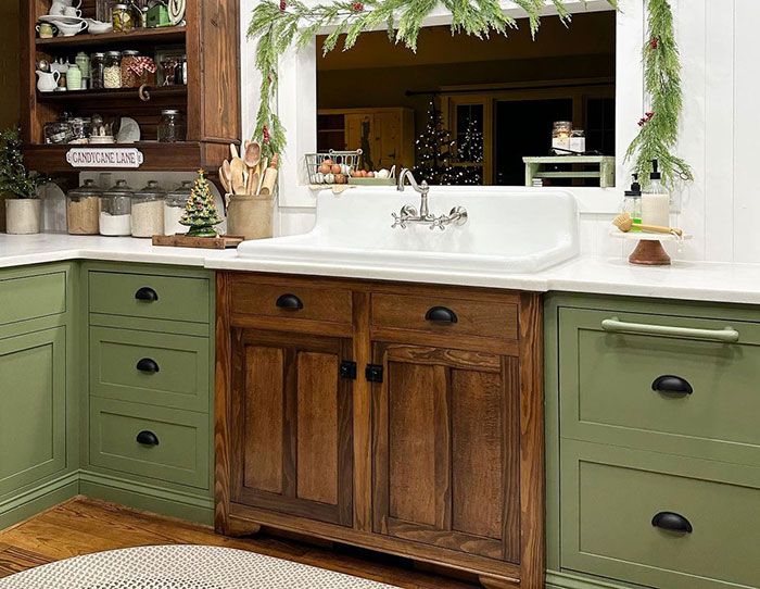 Green kitchen cabinets paired with brown wood cabinetry and white countertop in a cozy, naturally inspired kitchen setting.