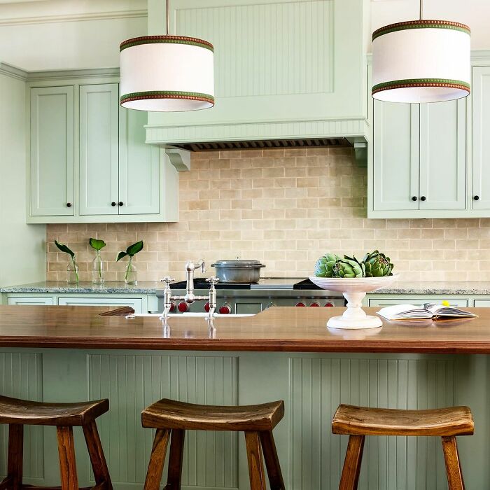 Light green kitchen cabinets paired with wooden countertops and stools in a bright, natural-colored space.