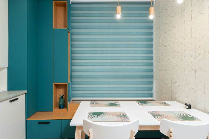 Teal green kitchen cabinets with white table and placemats in a modern dining space featuring natural colors.