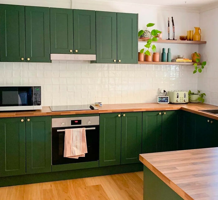 Green kitchen with green cabinets and wooden shelves, featuring natural tones and modern appliances in a cozy home setting.