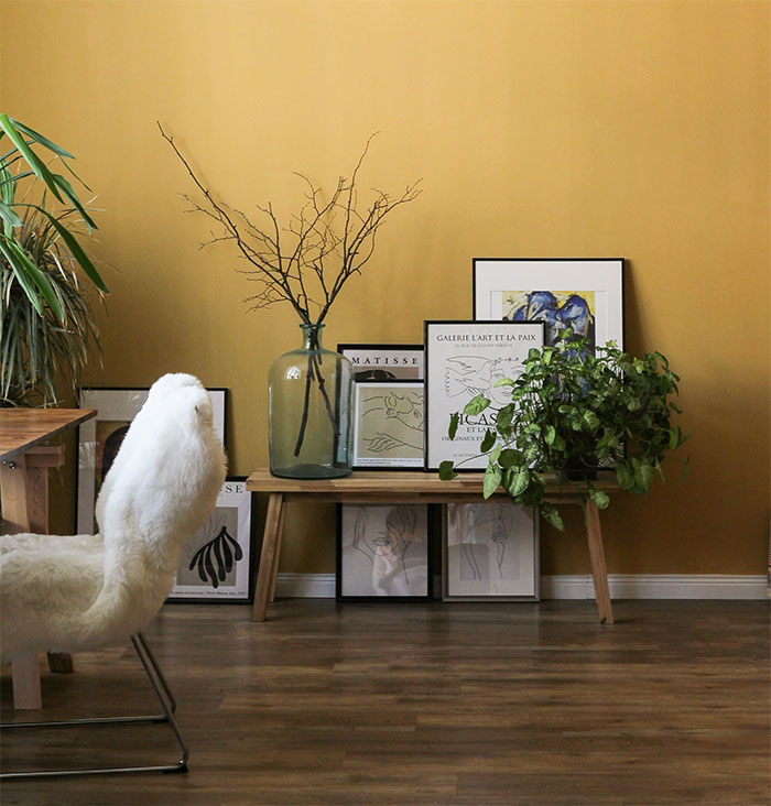 Pale yellow room with a fluffy white chair, framed art on the floor, and plants showcasing a happy color to transform your home.