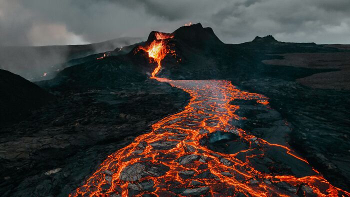 Erupted volcano with flowing lava under dark clouds, a powerful natural phenomenon.