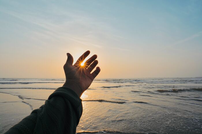 Left hand reaching towards the sunset over the sea, capturing a serene moment to ponder hard riddles.