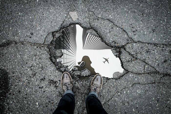 Person viewing complex reflection in a puddle, capturing a creative scene to challenge your wits with hard riddles.