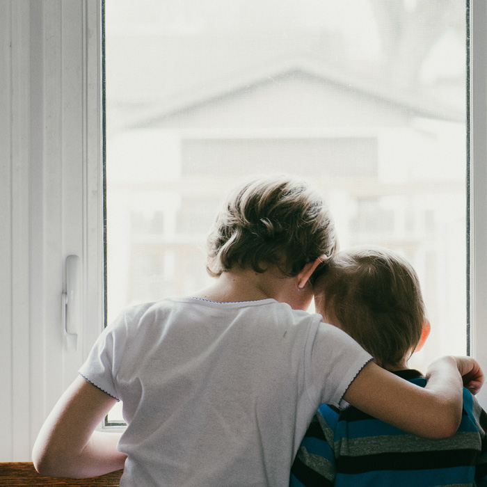 A kid wearing white t-shirt hugging another kid 