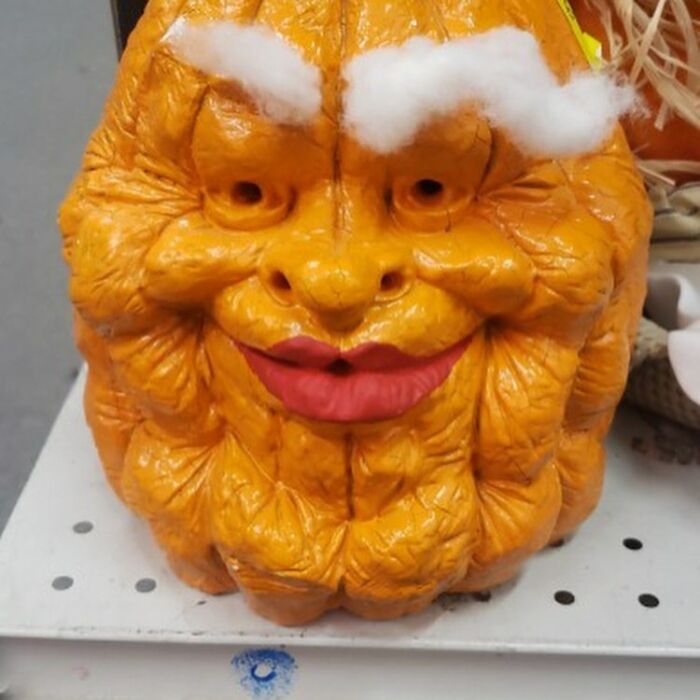 Odd thrift store item resembling a wrinkled orange face with cotton eyebrows and red lips on a store shelf.