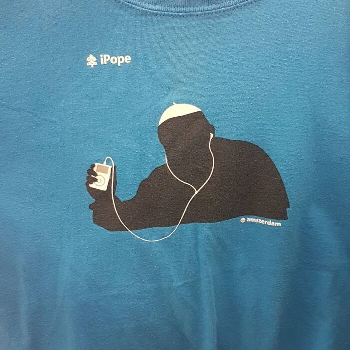 Blue shirt featuring a humorous graphic of pope silhouette holding an iPod, a weird item donated to thrift stores.