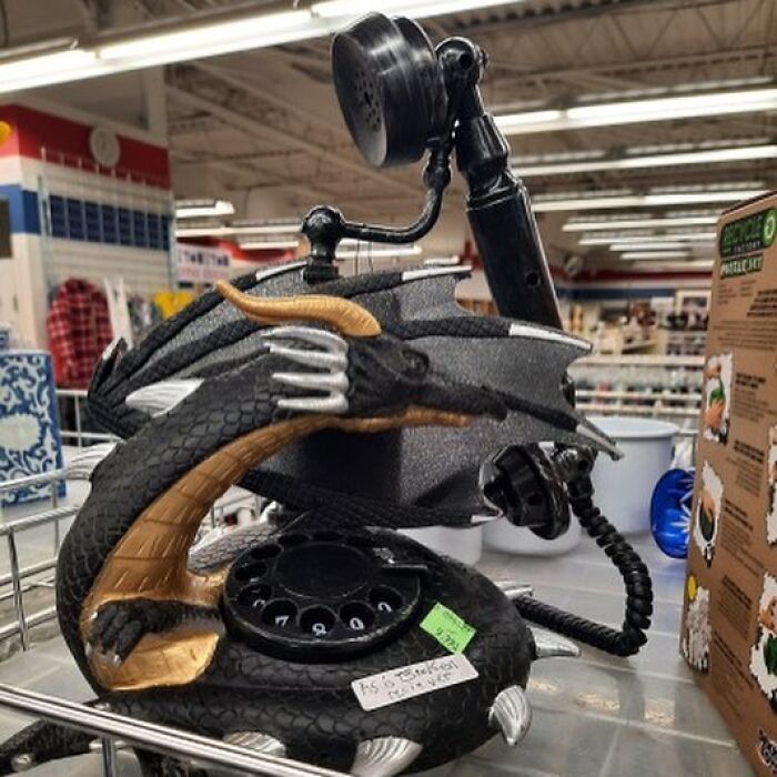 Black dragon-shaped rotary phone with gold and silver details displayed inside a thrift store with other vintage items.