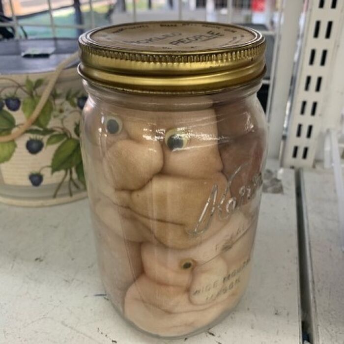 Jar filled with oddly shaped doll parts with googly eyes, one of the weird items donated to thrift stores.