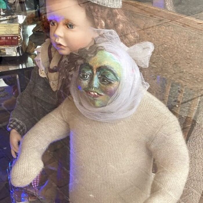 Two weird thrift store dolls displayed behind glass, one with a painted unusual face and fabric clothing.