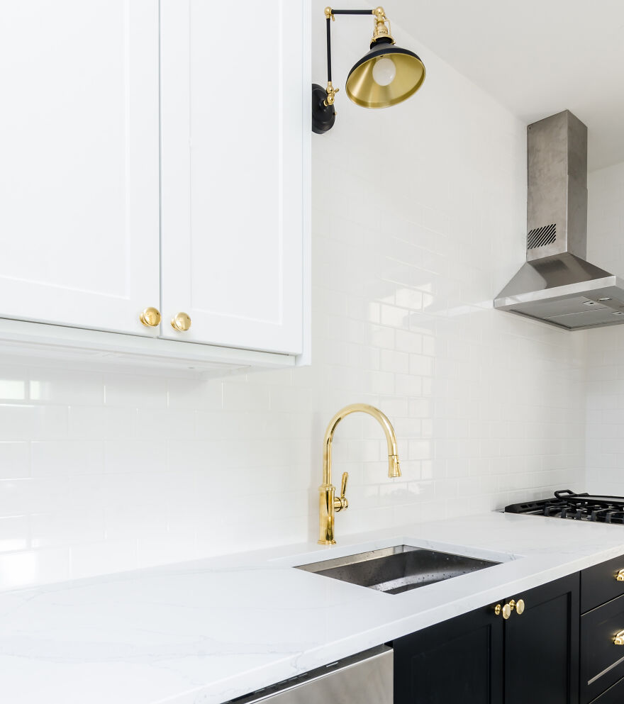White and black modern kitchen cabinets with gold hardware, a sleek faucet, and a stainless steel range hood in a stylish kitchen design