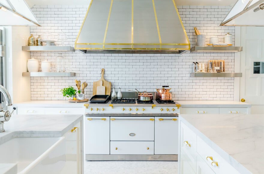 White modern kitchen cabinets with gold handles near stove oven in a stylish, bright renovated kitchen space