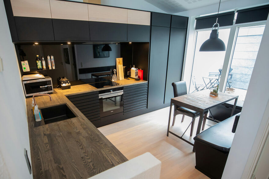 Modern kitchen with black cabinets and wooden countertops featuring a wooden table and natural light from large windows.