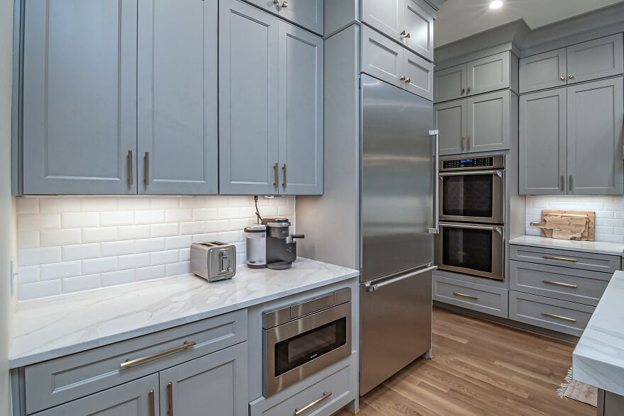 White and gray kitchen with modern and stylish kitchen cabinets, coffee maker, toaster, and stainless steel appliances.