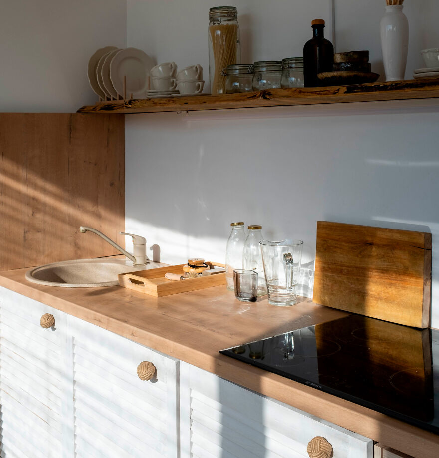 Modern and stylish kitchen cabinets with glass appliances and wooden countertop in a sunlit minimalist kitchen design