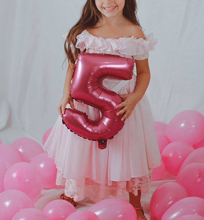 Young girl in a pink dress holding a birthday balloon surrounded by pink balloons, highlighting dress refusal at a birthday party.