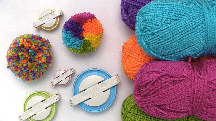 Pom pom makers and colorful yarn balls arranged on a surface, used as DIY tools for moss rugs and bath mats. Pom pom makers and colorful yarn balls arranged on a surface, used as DIY tools for moss rugs and bath mats.