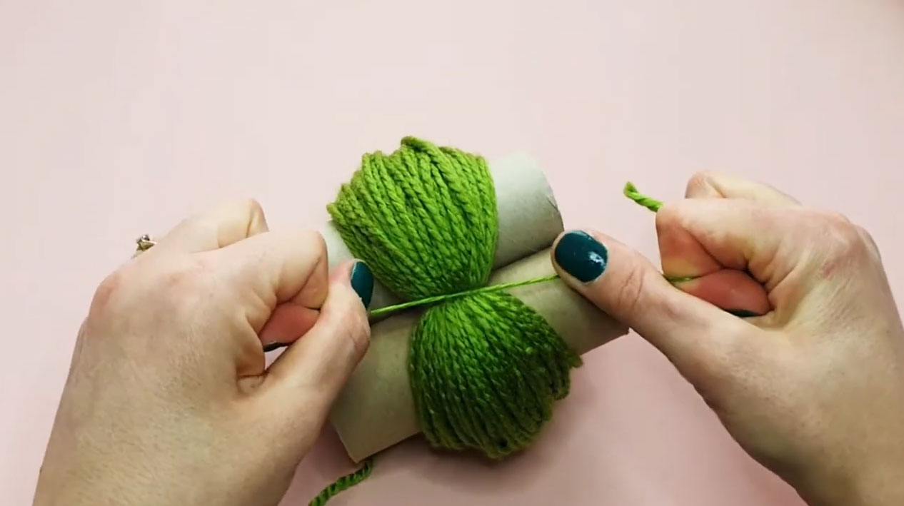 Hands making pom poms with green yarn wrapped around toilet paper rolls for DIY moss rugs crafting step. Hands making pom poms with green yarn wrapped around toilet paper rolls for DIY moss rugs crafting step.