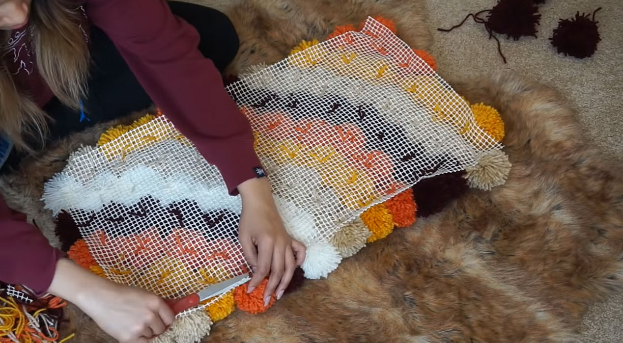 Person attaching colorful poms poms to a rug pad, demonstrating a step in making DIY moss rugs and bath mats. Person attaching colorful poms poms to a rug pad, demonstrating a step in making DIY moss rugs and bath mats.