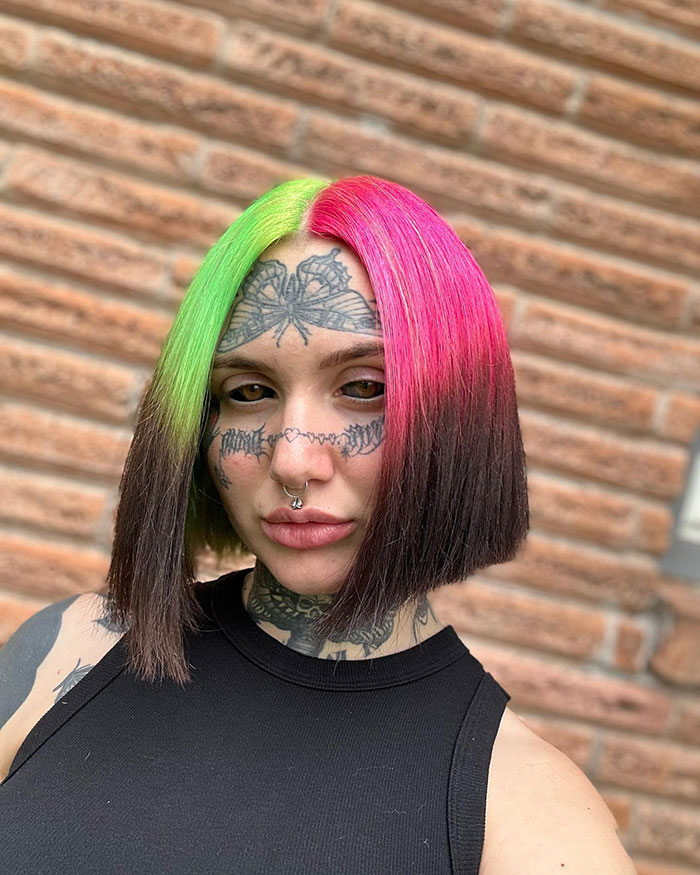 Woman with colorful hair and facial tattoos, showcasing inked look.