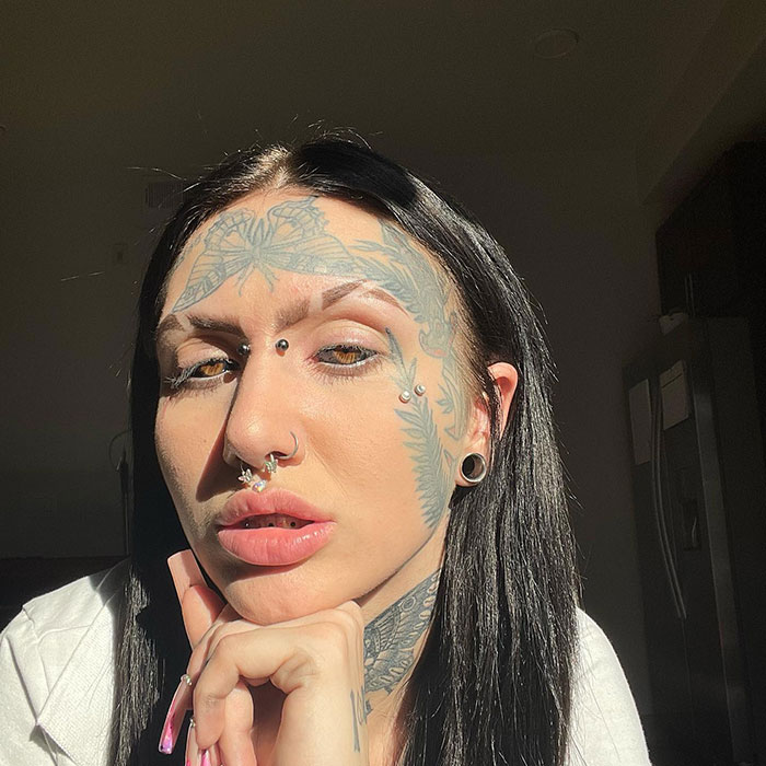 Woman with extensive inked body modifications shown in close-up portrait.