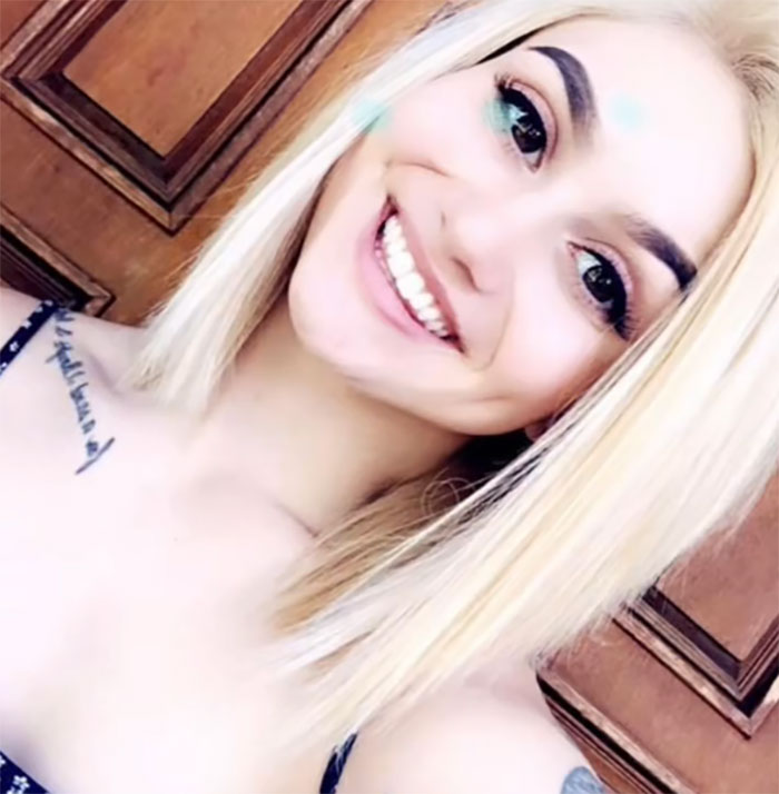 Woman with modified inked look smiling, displaying tattoos and piercings.