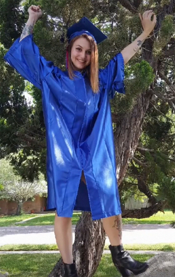 Woman celebrating in blue graduation robe, showing inked body modifications.