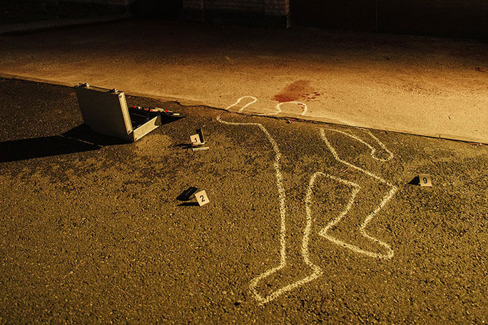 Chalk outline of a body at a crime scene with evidence markers and a briefcase, illustrating creepy facts about the world.