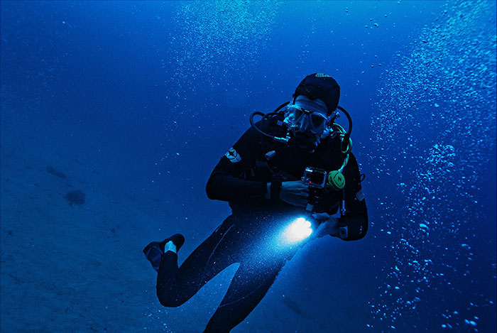 Scuba diver exploring dark underwater depths with flashlight, representing creepy facts about the world beneath the surface.