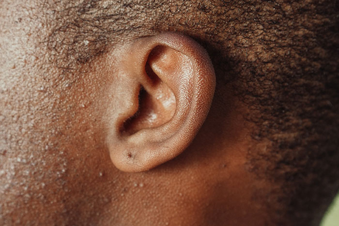 Close-up of a human ear with dark skin and textured hair, illustrating details for creepy facts about the world concept.