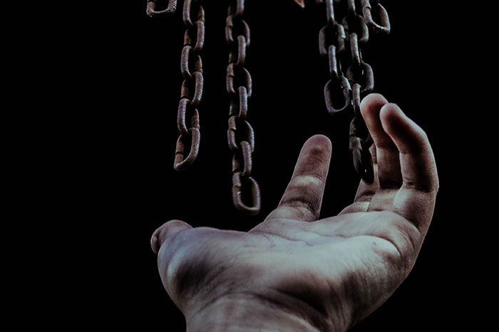 A hand reaching toward rusty chains hanging in darkness, evoking creepy facts about the world and unsettling mysteries.