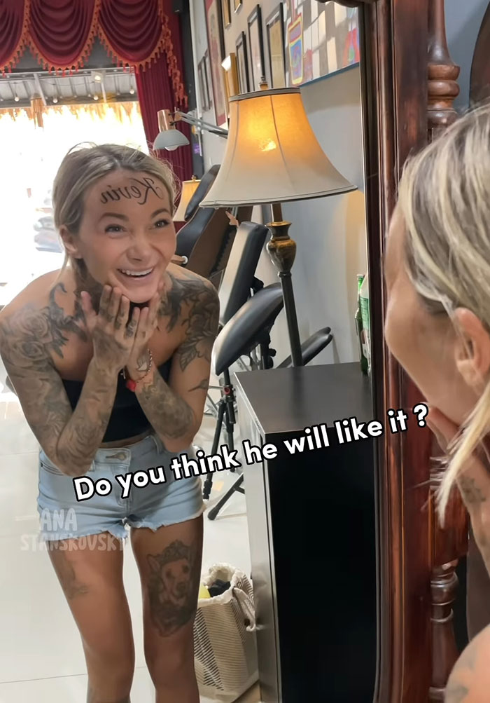 Influencer with boyfriend's name on forehead smiling at reflection, reveals ink is fake.