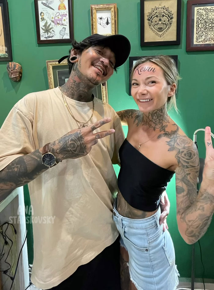 Influencer posing with &ldquo;Kevin&rdquo; inked on forehead, revealing it was fake, both smiling and surrounded by framed art.