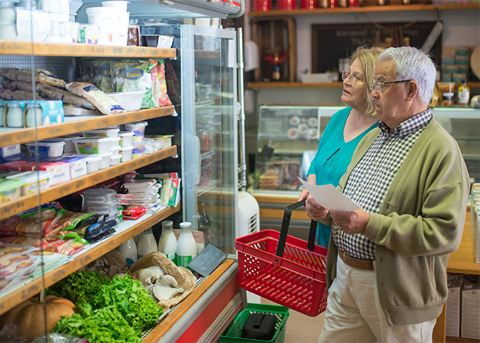 Older couple grocery shopping with a list in a store, illustrating lesser-known frugal tips with the biggest impact.