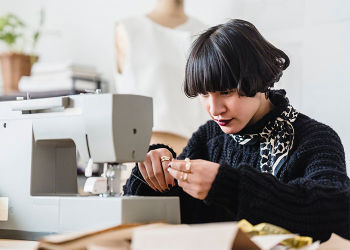 Young woman threading a sewing machine needle, demonstrating lesser-known frugal tips for cost-saving and budget impact.