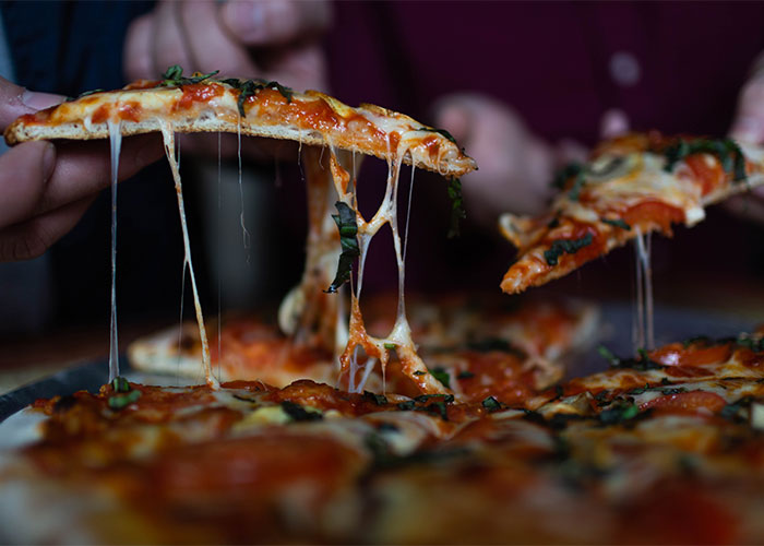 Close-up of hands pulling cheesy slices of pizza showing frugal tips for budget-friendly meal choices.