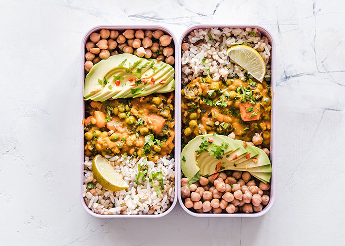 Two meal prep containers with rice, chickpeas, avocado slices, and a lentil vegetable curry, illustrating frugal tips for affordable meals.