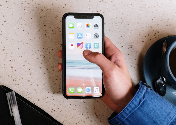 Hand holding smartphone with social media apps, illustrating lesser-known frugal tips for big savings shared online.