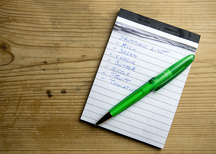 Shopping list on a notepad with a green pen on a wooden table, illustrating lesser-known frugal tips for saving money.