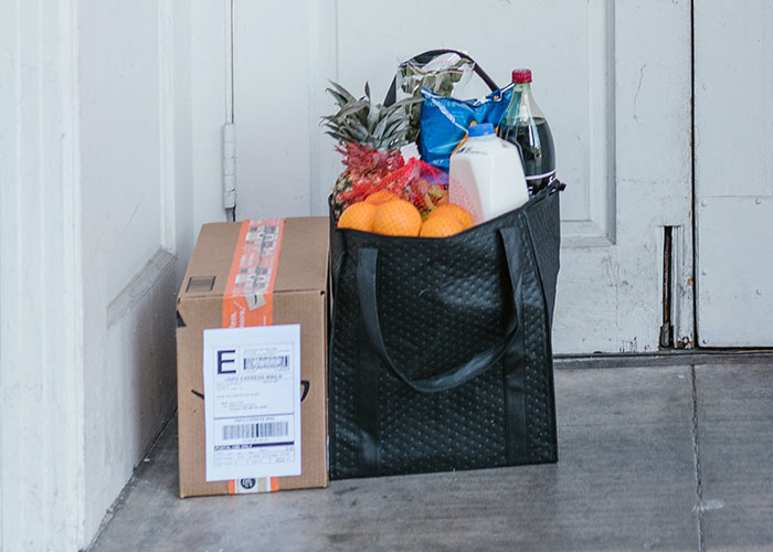 Reusable grocery bag filled with fresh produce and drinks beside a cardboard box, illustrating frugal tips for saving money.