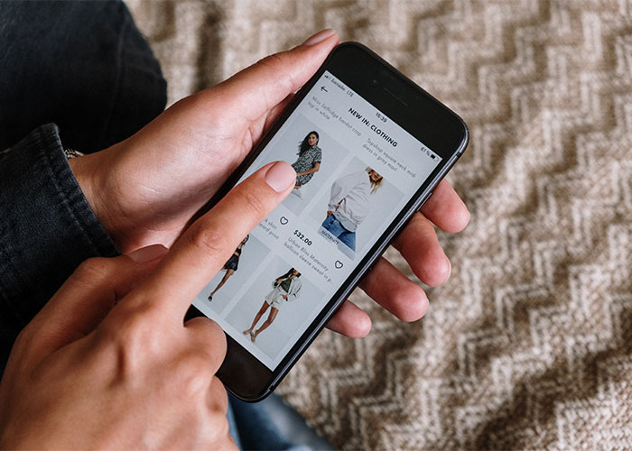 Person using smartphone to browse clothing online, illustrating lesser-known frugal tips for big impact savings.
