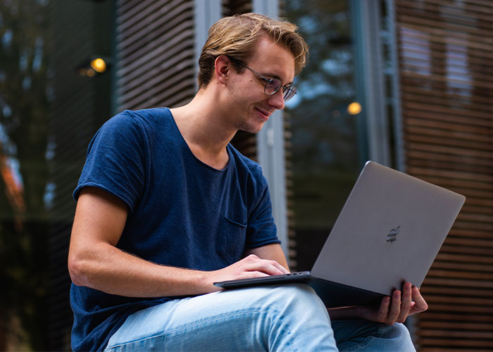 Young man in glasses using a laptop outdoors, researching lesser-known frugal tips with biggest impact in casual setting
