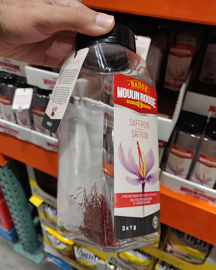 Hand holding a saffron spice container with a packaging fail where saffron is stuck in the bottom corner plastic area.