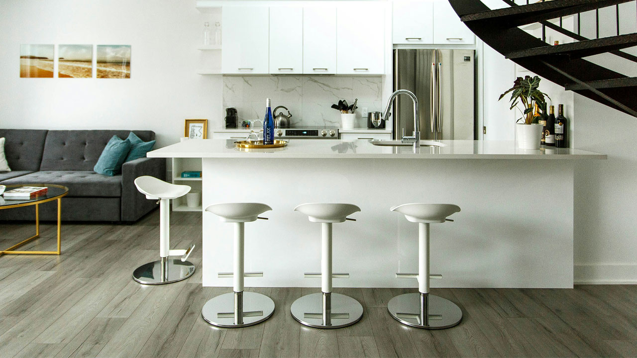 Modern kitchen featuring sleek white kitchen cabinets and a large island with white bar stools in a minimalistic space Modern kitchen featuring sleek white kitchen cabinets and a large island with white bar stools in a minimalistic space