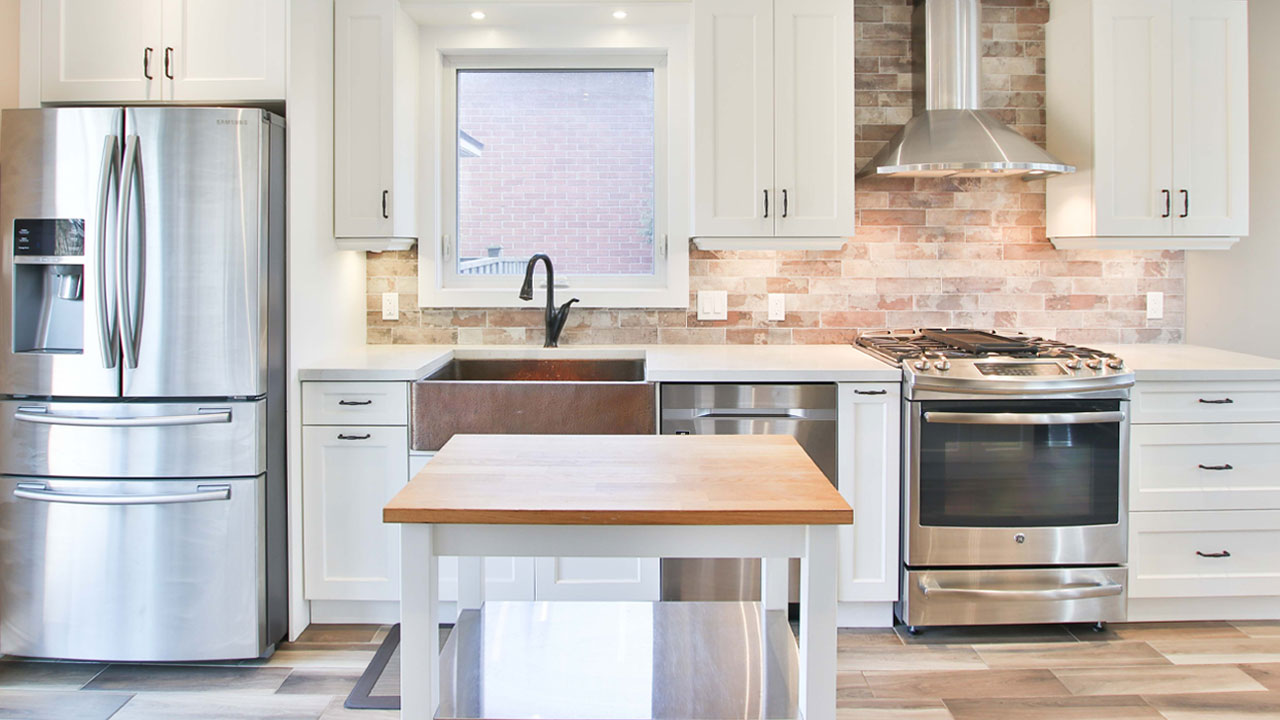 Industrial kitchen featuring white kitchen cabinets, stainless steel appliances, brick wall backsplash, and a wooden island. Industrial kitchen featuring white kitchen cabinets, stainless steel appliances, brick wall backsplash, and a wooden island.